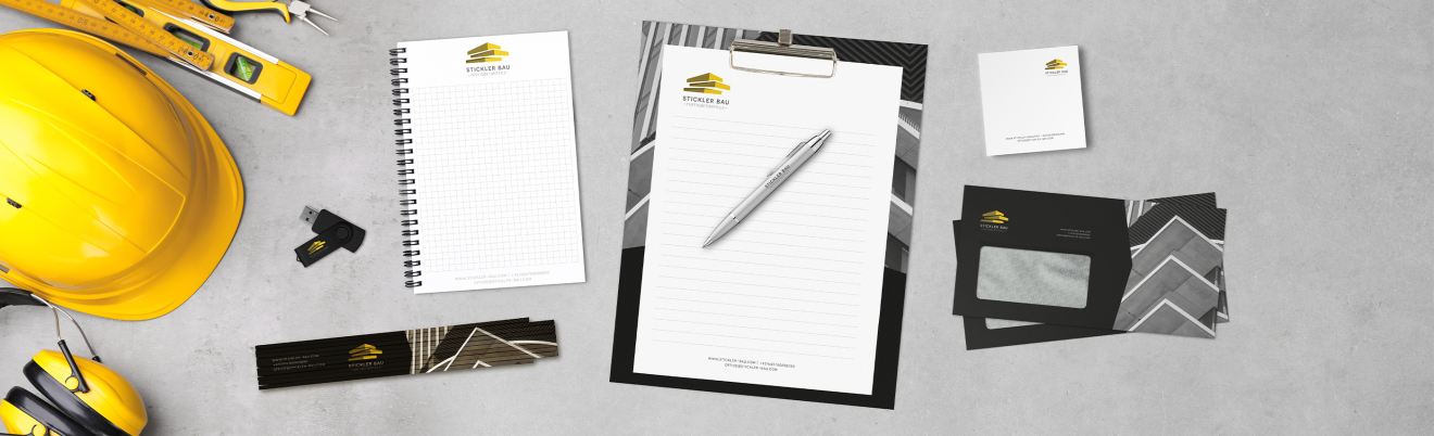 Ein flaches Layout mit Schreibwaren aus dem Baugewerbe, darunter ein Schutzhelm, ein Maßband, ein Notizblock, ein Klemmbrett mit Papier und Stift, Visitenkarten, Briefumschläge und ein Lineal, alle mit einem gelb-schwarzen Baulogo versehen.