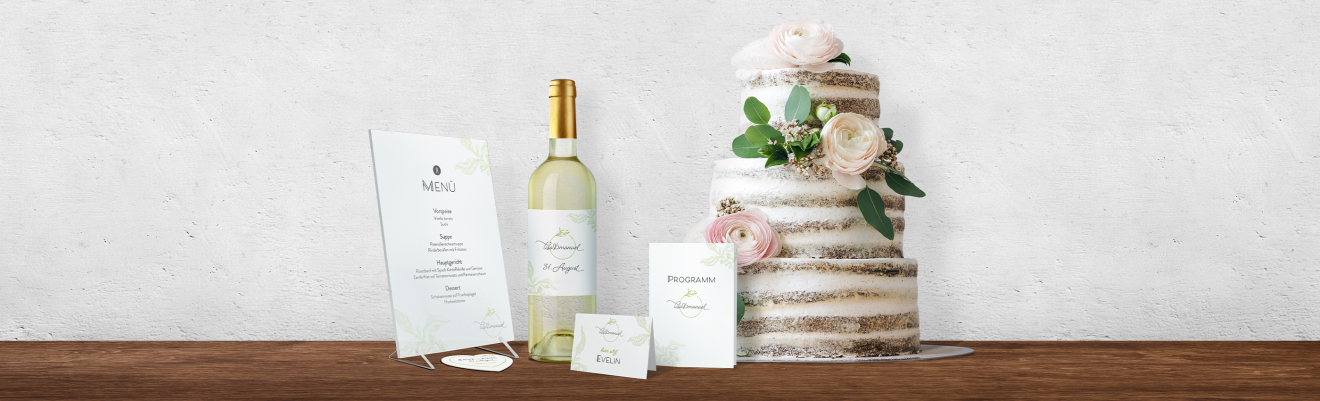Eine rustikale, halbnackte Hochzeitstorte, verziert mit weißen und erröteten Blumen, steht auf einem Holztisch neben einer Flasche Weißwein und eleganter Hochzeitspapeterie, darunter ein Menü, eine Tischkarte, ein Programm und eine Dankeskarte.