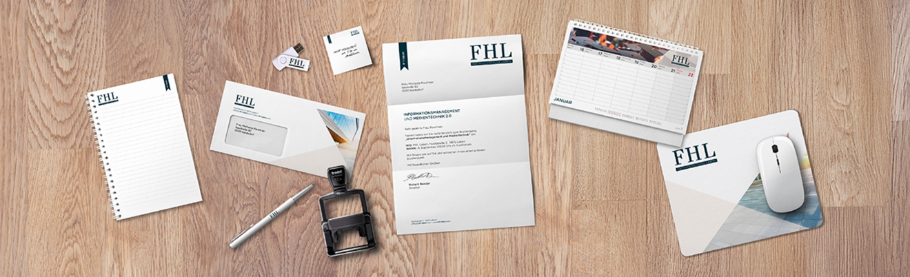 Ein Set von Marken-Büroartikeln auf einer hölzernen Oberfläche, einschließlich eines Notizblocks, Umschlägen, Visitenkarten, eines Stifts, eines Stempels, eines Briefbogens, eines Kalenders und eines Mauspads, alle mit dem FHL-Logo und einem abgestimmten Design.