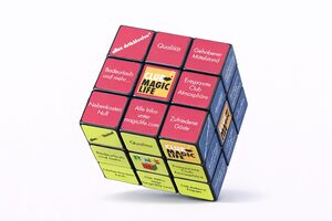 Ein Rubik's Cube, bei dem die Flächen durch gebrandete Quadrate mit Clubmotiven ersetzt wurden, darunter Sätze auf Deutsch wie "Qualität", "Club MAGIC LIFE", "Entspannte Club-Atmosphäre" und bunte Abschnitte.