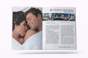 Aufgeschlagenes Magazin, das auf der linken Seite ein lächelndes Paar zeigt, das zusammen unter weißen Laken liegt, und auf der rechten Seite Informationen mit Fotos von Menschen in einem Ferienort mit dem Titel Kemer Imperial.