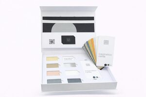 Eine offene Präsentationsbox enthält Farbmuster, beschriftete Materialproben, mehrere Karten mit der Aufschrift "Inspiration Cards" und einen QR-Code auf weißem Hintergrund.